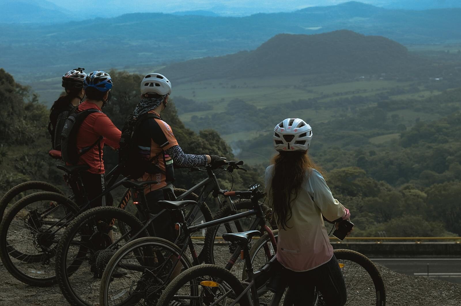 A group of cyclists stand on a hilltop enjoying a breathtaking mountain view, equipped with helmets and bikes.