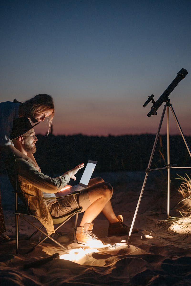 A couple enjoys a peaceful evening stargazing with a telescope and laptop at twilight.